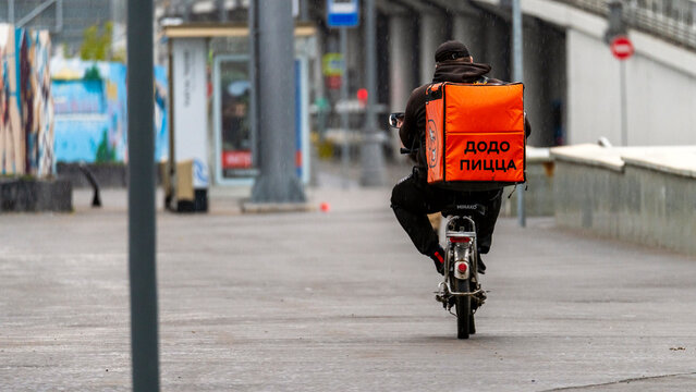 Moscow July 17, 2023, Dodo pizza delivery, Courier on a bicycle with an orange backpack for groceries.