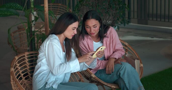 On bench young friends converse phone in hand showcasing women's communication. Women's communication reflects genuine smiles laughter Women's communication essence camaraderie positivity.