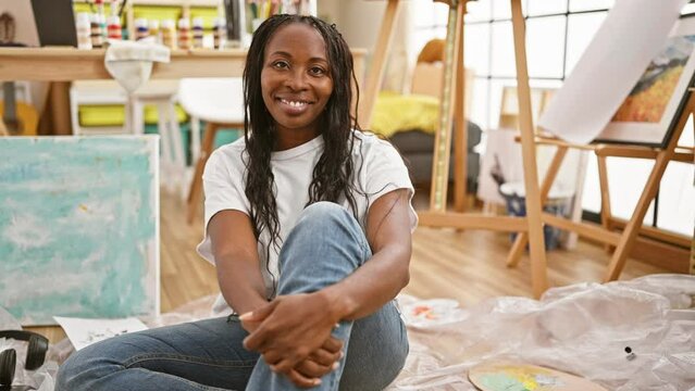 African american woman with curly hair sitting relaxed in a creative studio environment, smiling at the camera