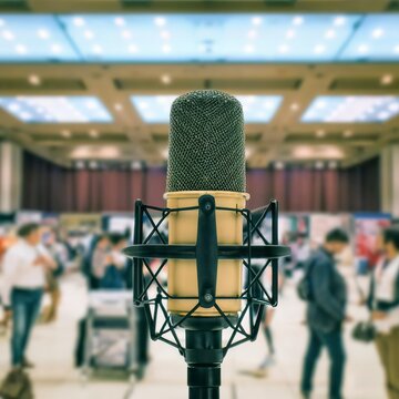 Close up of old vintage style podcast microphone in convention hall and blurry people background