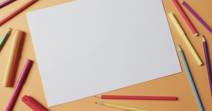 Overhead view of blank sheet of paper with school stationery on beige background, in slow motion
