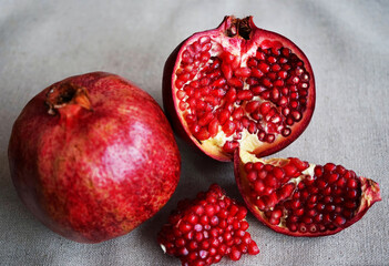 A cut pomegranate next to a whole one on a gray background