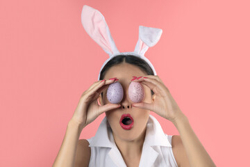 Beautiful young woman with pink bunny ears holding a colorful Easter eggs in front of her eyes. Minimal Easter concept.