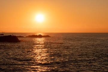 オレンジ色の朝日に染まる磯と海