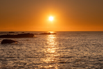 Obraz premium オレンジ色の朝日に染まる磯と海