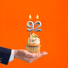 Hand holding birthday cupcake with number 92 candle - background orange