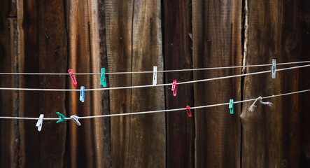 Colorful clothespins hanging on washing line or rope against the background of a wooden fence.
