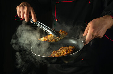 The cook is preparing fish in the kitchen. The concept of preparing a fish dish for breakfast. The chef hand uses tongs to remove hot fried carp from the frying pan