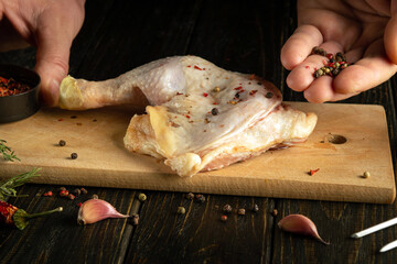 Cooking chicken leg. The cook adds dry pepper to the broiler leg with his hands for flavor and aroma before roasting