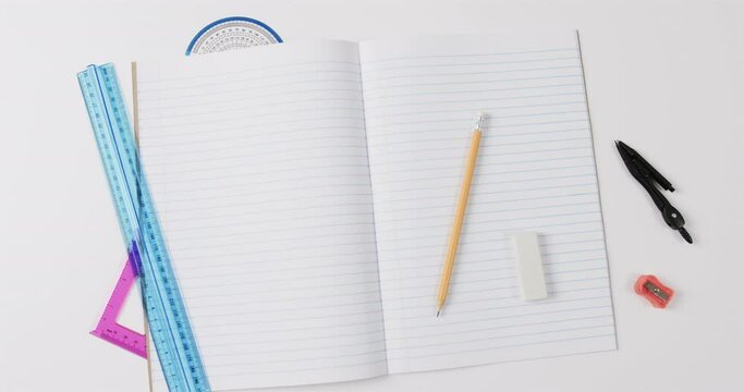 Overhead view of open notebook with school stationery on grey background, in slow motion