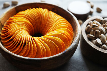Potato chips and pistachios in wooden bowls next to sauce on gray background