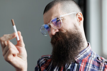 Brutal man with a cigarette on a blurred background in a gray room. Stop smoking concept.