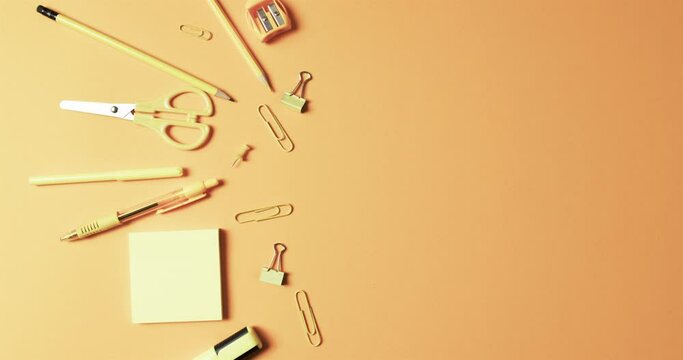 Overhead view of school stationery with copy space on orange background, in slow motion