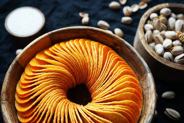 Potato chips and pistachios in wooden bowls next to sauce on a dark background