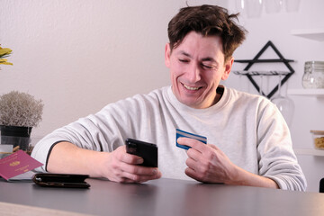 Pleased happy man with on the phone with a credit card in hand, passport and wallet on the table