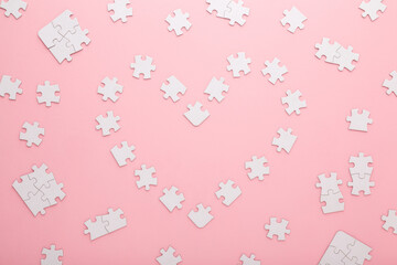Heart shape created from white puzzle pieces on light pink table background. Pastel color. Closeup. Love and relationship concept. Top down view.