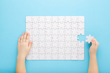 Little kid hand holding and putting last one white puzzle piece on light blue table background....