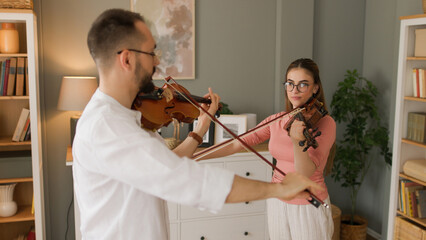 Male violin teacher plays a piece with young female student