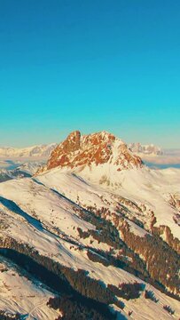 Aerial helicopter shot of calm rural mountain landscape, snow-covered mountain peaks and ski resort landscape at the Austrian Alps on a sunny afternoon day. vertical video