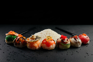 Variety of bright sushi rolls with greens on a black background. Incredible fresh sushi rolls on a dark background. Cooking traditional Japanese seafood and fish dishes.