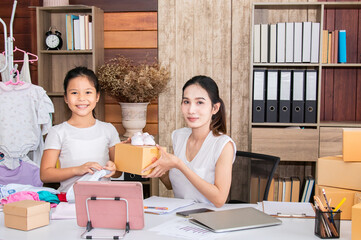Asian parent working while looking after a young baby or toddler, single mother businesswoman working from home multitask nursing infant using technology modern laptop online selling children clothes