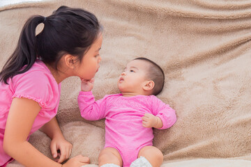Asian sibling love bonding relationship, adorable girl playing with toddler younger sister on bed...