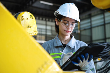 Caucasian female robotic engineer wearing helmet and safety glasses using tablet to check the operation of industrial robot arm in factory. - obrazy, fototapety, plakaty
