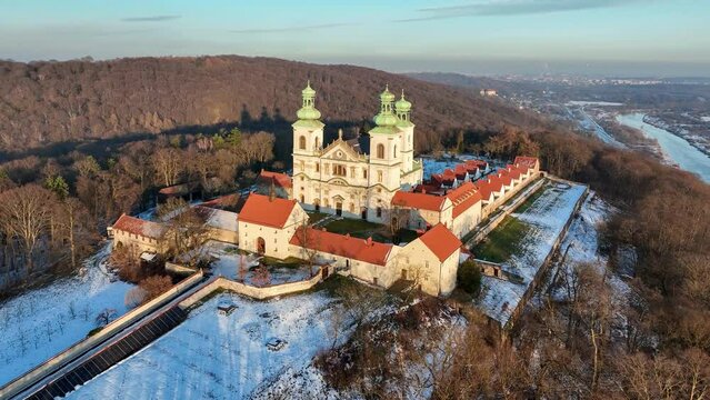 Camaldolese monastery and baroque church in the wood on the hill in Bielany, Krakow, Poland , Aerial 4K video in sunset light in winter. Far view of Vistula River and Cracow city in the background