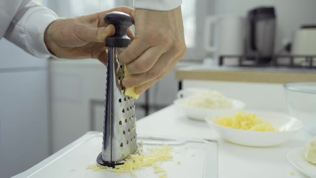 A man is grating cheese on the table. Close-up.