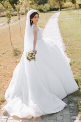 Photo from the back. A beautiful young woman in a white wedding dress is smiling on a warm wedding summer day