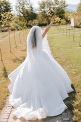 Photo from the back. A beautiful young woman in a white wedding dress is smiling on a warm wedding summer day
