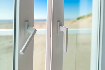 Sliding door from a balcony to the beach. Closeup of door lock with nice and sunny seascape in background. White PVC door and safety glass.