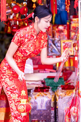 Asian woman in red cheongsam dress choosing and buying home decoration and ornament for celebrating Chinese Lunar New Year festival at market.Celebrate Chinese lunar new year.Celebrate season holiday.