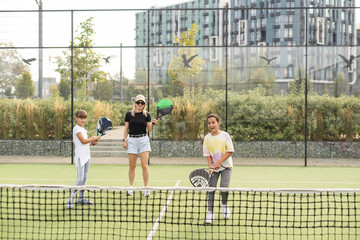 Young sporty woman with children playing padel game in court on sunny day