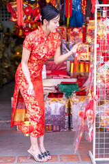 Obraz premium Asian woman in red cheongsam dress choosing and buying home decoration and ornament for celebrating Chinese Lunar New Year festival at market.Celebrate Chinese lunar new year.Celebrate season holiday.