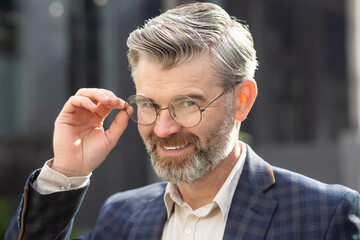Smiling senior expert with a distinguished beard adjusting his glasses successful mature man in a...