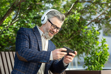 Fototapeta premium Mature executive in business attire relaxes with music outside office, combining leisure with corporate lifestyle.