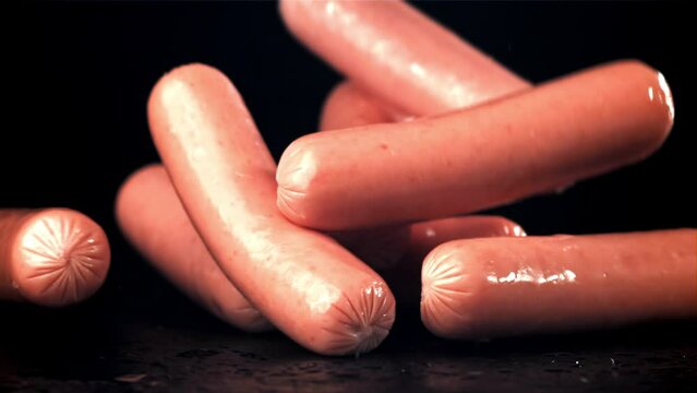 Fresh sausages fall on a wet black table. Filmed on a high-speed camera at 1000 fps. High quality FullHD footage