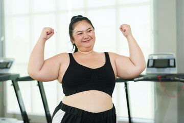 Overweight Asian woman exercise in gym, Exuberant  flexing muscles, showing strength and joy, treadmill machines in behind, flexing biceps, displaying strength and happiness in fitness setting