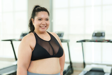 Plus-size Asian woman exercise in gym, Smiling apparel stands confidently in a fitness center, with...