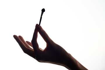 Close-up of a silhouette of a blush brush in a woman hand on a white background.