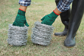 Close up worker hand wear green gloves, holds rolls of barbed wire. Concept, construction tool....