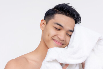 Obraz na płótnie Canvas A serene young Asian man with a smile, drying his face with a fluffy white towel, eyes closed in satisfaction.
