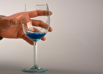 niebieski płyn w peknietym kieliszku do wina, dłoń trzymajaca pęknięty kieliszek, blue liquid...