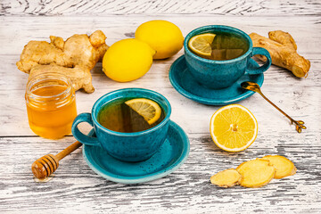 Two blue cups and ingredients for ginger tea, honey, lemons, ginger root on wooden background, side view