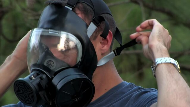 A solider puts on his gas mask in the forest.