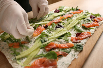 Salmon and cucumbers are added to lavash with cheese and greens. Preparation of a roll with cheese, fish and vegetables