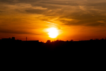 Orange and red sky backlit by trees at dawn or dusk in a rural area
