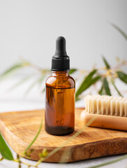 Nail oil or serum in a bottle on a wooden board with a brush on a gray background with green leaves. © Kufotos