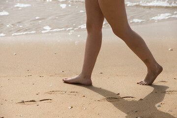 Legs and feet of a woman walking on the sand of the beach with the water of the sea in the background.